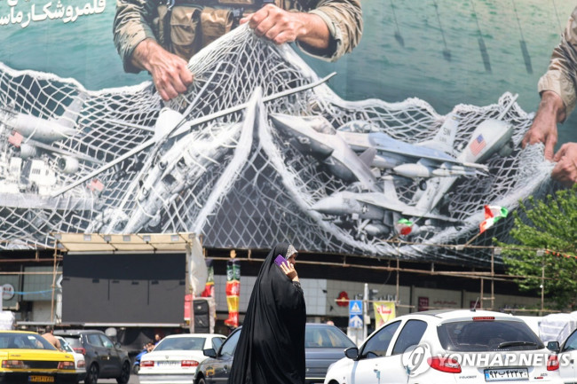 이란 테헤란 거리에 걸린 선전화 앞을 지나는 여성의 모습